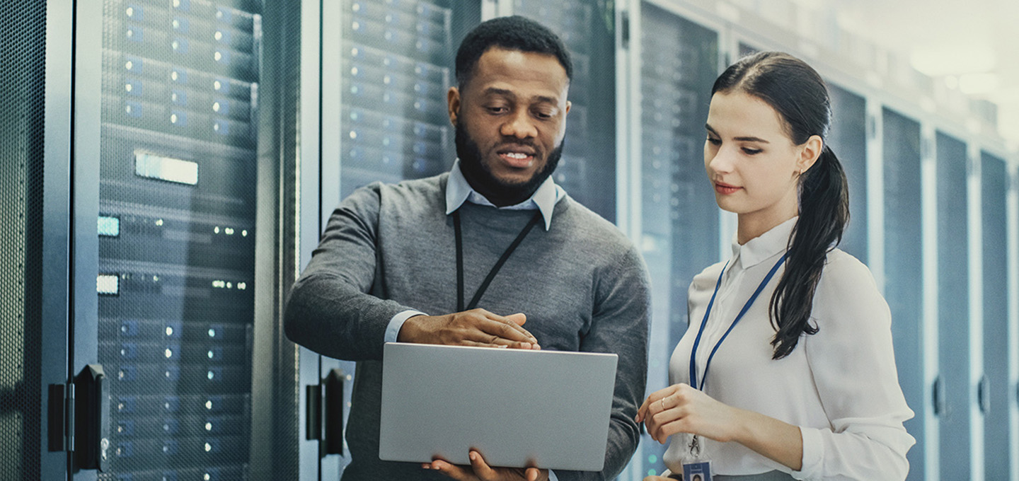Man explaining something to woman standing at laptop