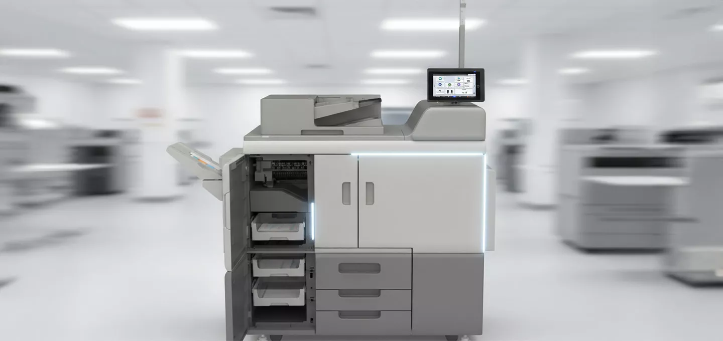 A gray and white Ricoh Pro 8400s Series printer with its front panel open, revealing paper trays and internal components. The printer has a touch screen on top. The background is a brightly lit, blurred office or print room.