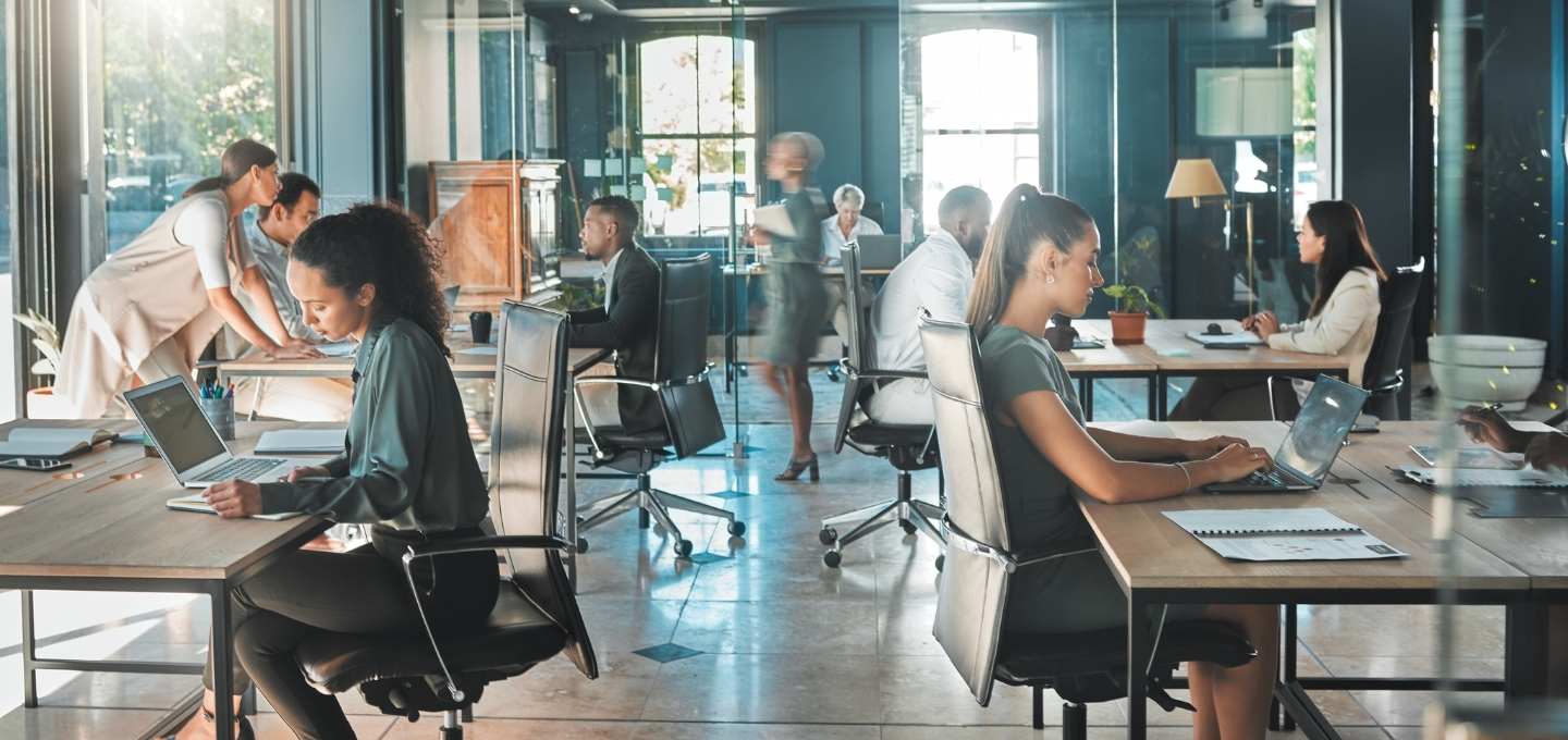 Modern workplace with professionals collaborating and working at desks in an open office environment, representing Ricoh spaces.